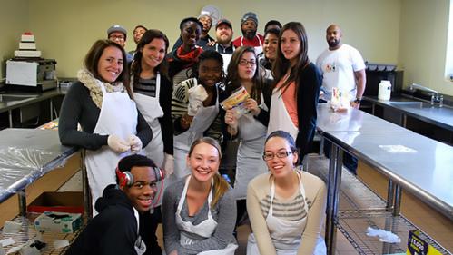 Diverse group of male and female students smiling while volunteering in a community kitchen