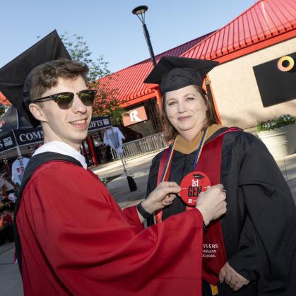 A graduate pins a first generation badge on his mother’s graduation gown at commencement