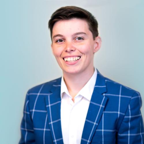 Brittany has short cropped hair and is wearing a blue and white checkered suit and a white collared inside shirt.