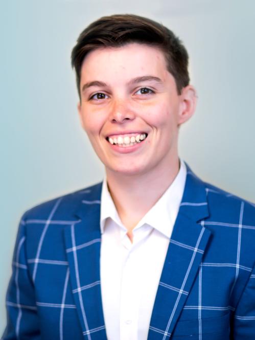 Brittany has short cropped hair and is wearing a blue and white checkered suit and a white collared inside shirt.