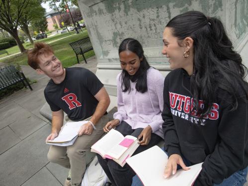 Students sit beneath a statue on campus and study textbooks
