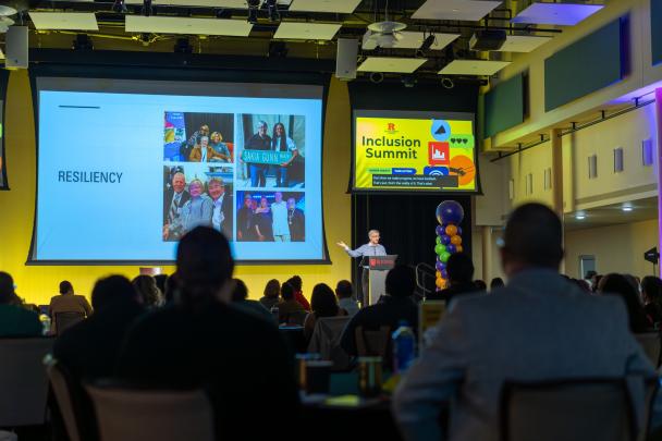 A crowd of people watching a presenter show a slide on a stage