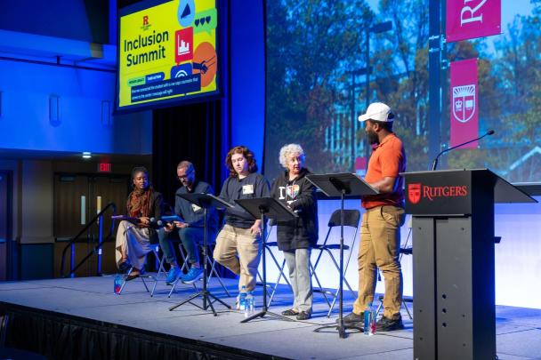 Panelists on a stage in front of a screen with an image of the outdoor campus