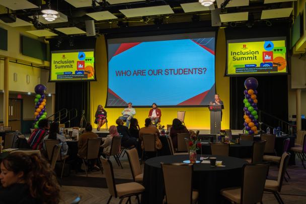 Panelists seated on stage with a moderator at a podium in front of a large crowd