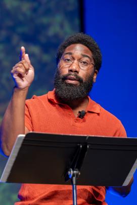 A speaker standing at a podium and pointing a finger upward